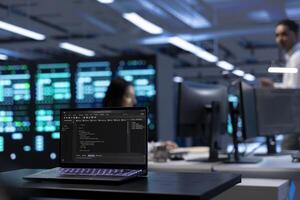 Focus on laptop used by IT developer in server room to find network issues affecting supercomputer performance and connectivity, leading to slow data transfer rates and poor client communication photo