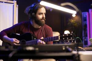 Musical artist mixing and mastering guitar tunes played on acoustic instrument, using electronic controls on console and daw software. Songwriter producer creating new sounds, home studio. photo