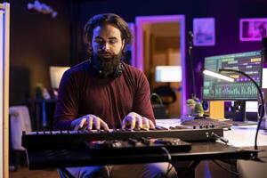 Skilled producer creating new music on piano midi controller, working with mixing console and daw software interface on pc. Musician artist singing at microphone and mastering acoustical tunes. photo