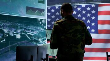 Professionals in US military uniforms operate computers and big screen, working on surveillance and intelligence to ensure national security from a high tech control center. Camera A. photo