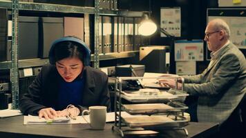 Private detective extracting important ideas from witness statements, taking notes based on classified documents. Forensic expert looks into archived legal documents, listens to music. Camera A. photo