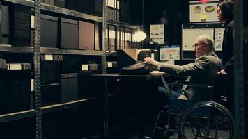 Detective with impairment develops case timelines and profiles using archival records and research, disability friendly archive room. Senior agent in wheelchair interpreting legal files. Camera B. photo