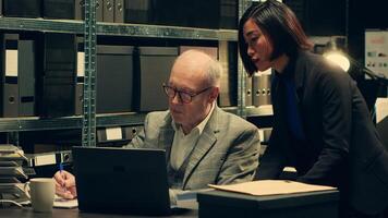 Senior inspector showing case details to his partner in archive room, studying forensic evidence and classified criminal records in a box. Detectives team work on federal investigation. Camera A. photo