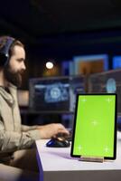 Focus on chroma key tablet with sentient AI in blurry background gaining humanoid form. Isolated screen device next to self aware artificial intelligence on PC discussing with engineer, close up photo