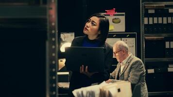 Private investigator organizes archived files for easy access, searching for old file cases to cross reference data. Law enforcement agent looking for classified folders in archive room. Camera B. photo