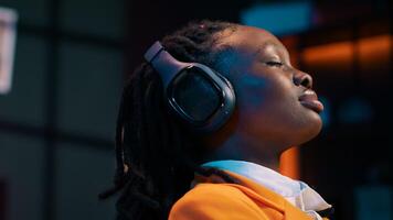 Carefree student finishes creating a presentation and relaxes with music on audio headset, resting after long researching session. African american girl chilling with ambience tunes. Camera A. photo