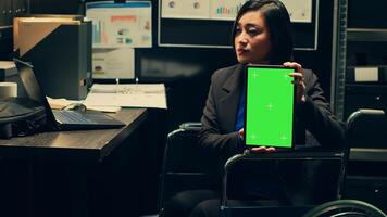 Detective wheelchair user holds greenscreen layout on tablet, using copyspace isolated display on gadget in incident room. Private investigator holding device with mockup screen. Camera A. photo