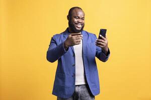 Upbeat man giddying in excitement while adding payment method on phone, enjoying himself, studio background. Ecstatic person satisfying urges with internet shopping, typing credit card information photo