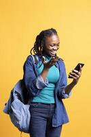 Woman using smartphone laughing at hilarious social media posts on feed. Jolly african american girl browsing internet websites, amused by funny memes, isolated over studio background photo