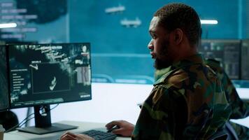 Team of military specialists overseeing surveillance activity by using a cctv footage and radar, pointing at a big screen and world map. High tech control center base of operations. Camera A. photo
