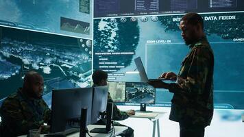 Military officers work in a high tech army control tower base, managing surveillance imagery from cctv satellite. Soldiers handle data protection to ensure national security. Camera B. photo
