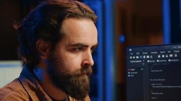 Software technician in apartment office deeply immersed in coding on computer at desk, close up. IT freelancer absorbed by work, focused on screen, writing lines of code at workstation, camera A photo