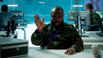 Military officer participates in a secure videoconference call in modern command center, transmitting live satellite information. Federal collaboration for national security operations. Camera A. photo