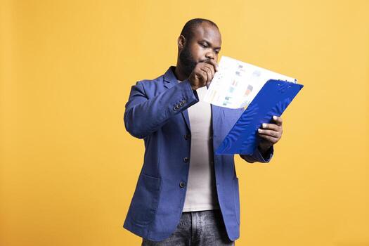 Man browsing though audit report pages, isolated over studio background. Employee reading clipboard with files containing economic graphs and figures, solving company tasks photo
