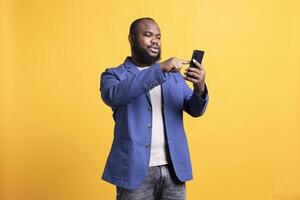 BIPOC man texting best friend using smartphone, reading messages. Relaxed african american person having fun while chatting with mate on mobile phone, isolated over studio background photo