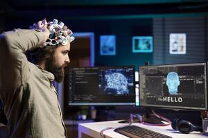 Man placing EEG headset on head to communicate with artificial intelligence entity with anthropomorphic body. Software programmer using high tech gear to talk with AI robot in humanoid form photo