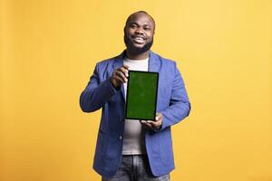 Portrait of man doing influencer marketing using isolated screen tablet, showing positive emotion, studio background. Merry BIPOC person holding empty copy space mockup portable gadget photo