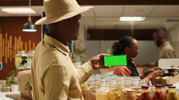 Small business owner uses greenscreen layout on smartphone app, presenting isolated display with copyspace template. Local farmer holding phone with blank mockup chromakey screen in store. Camera 1. photo
