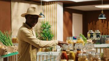 African american client shopping for pasta or grains in jars, looking at variety of bulk products stored in reusable containers. Buyer supporting eco friendly business, nonpolluting goods. Camera 1. photo