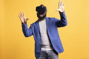 Tech enthusiast wearing virtual reality goggles, doing swiping gestures. BIPOC man using high tech futuristic modern VR glasses, making tactile touching gesturing, studio background photo