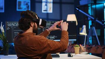 Remote software developer using VR goggles in personal office at home to do javascript programming. IT engineer wearing virtual reality headset in order to visualize lines of code, camera A photo