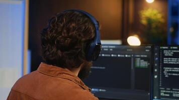 Man doing IT support job from apartment office, drinking cup of coffee and listening music while coding. Developer with headphones on enjoying hot tea and writing code on computer, camera A close up photo