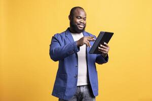 Smiling man adding payment method on website, enjoying sales period, isolated over studio background. Upbeat man doing internet shopping, typing credit card information on tablet photo