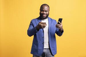 Upbeat man adding payment method on phone, enjoying himself, isolated over studio background. Joyous person delighted to do internet shopping, carefully typing credit card information photo