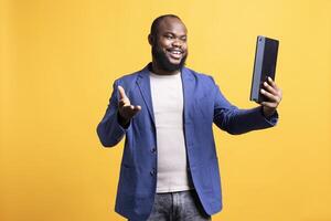 Smiling man excited to talk with friends during teleconference meeting using tablet, isolated over studio background. Happy person having discussion with mate during internet call on device photo