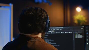 Technician putting headphones on while using coding to fortify firewalls, teleworking for IT company. Computer scientist listening music and upgrading binary code scripts in home office, camera A photo