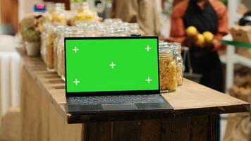 Computer showing blank chromakey display next to goods in jars, local grocery store supporting organic farming and sustainable lifestyle. Modern laptop running greenscreen isolated layout. Camera 1. photo