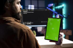 Admin doing software debugging using isolated screen tablet, checking errors in lines of code displayed on PC monitors. Man working from home fixing coding issues using chroma key portable device photo