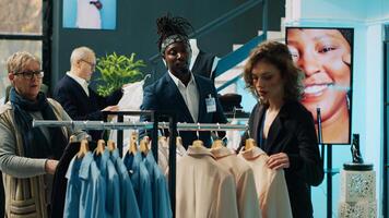 Employees team presenting variety of clothes to senior client, helping her to choose the perfect shirt size to create a formal outfit. Diverse store assistants show clothing from designers. Camera A. photo