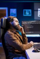 Bored programmer fixing vulnerabilities in software enabling hackers to compromise systems, waiting for shift to end. Impassive man wearied by job, using PC to patch security exposures photo