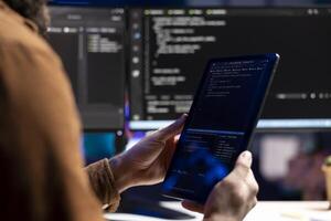Computer scientist doing software quality assurance using tablet, reading source code before implementing it. Developer inspecting coding on portable device, looking to fix potential issues photo