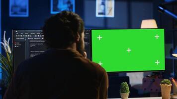 Programmer typing complex code on green screen computer in neon lit home office, developing software application. Teleworking IT specialist doing remote project tasks on mockup PC monitor, camera A photo