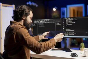 Angry programmer trying to smash keyboard in frustration after failing to secure company servers from virus attacks. Irritated man releasing pent up emotions, unable to build firewalls protecting data photo