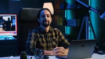 Portrait of happy man sitting at home office desk, preparing to solve tasks on laptop. Cheerful freelancer in front of digital device, doing email communication in living room, camera A photo