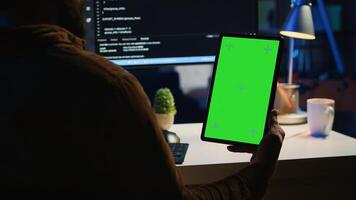 Software developer programming in home office, crosschecking lines of code between green screen tablet and PC screen. IT admin holding mockup portable device while coding on computer photo