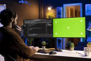 Freelancing admin using green screen computer monitors to filter malicious traffic from cybercriminals attempting to corrupt company data. IT expert in apartment working on mockup desktop PC photo