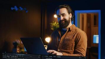 Portrait of smiling man doing IT support job from home, standing in personal office with laptop in hand, coding. Cheerful programmer writing lines of code on notebook in living room, camera A photo