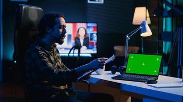 Man in home office checking statistical data financial graphs on documents files, crosschecking with mockup laptop. Remote employee comparing business graphics paperwork with green screen device photo