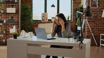 Stressed overworked indian employee struggling to concentrate while working from home, hurting from headache. Tired teleworker feeling nausea while working on laptop, camera A photo