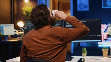 Software engineer writes binary code scripts on computer and drinks coffee. IT specialist in home office enjoying hot beverage while using programming to safeguard consumer data, camera A photo