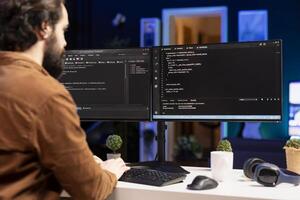 IT expert working from home developing software in JavaScript programming language using desktop PC. System engineer in living room writing lines of code on computer using keyboard photo