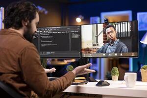 Programmer doing software debugging helped by coworker in videocall, checking errors in lines of code. Man working from home fixing coding mistakes, assisted by colleague in teleconference photo