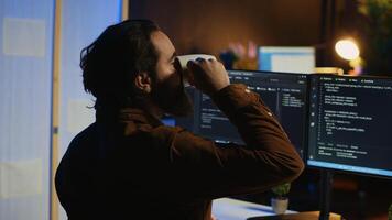 Computer scientist at home office desk writes binary code scripts and drinks from mug of coffee. IT expert in apartment enjoying tea while using programming to safeguard consumer data, camera A photo