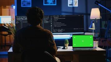Programmer coding on computer next to isolated screen laptop in home office, developing software application. Teleworking IT specialist doing programming on PC near chroma key notebook, camera A photo