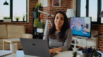 Portrait of indian teleworker checking her emails on laptop while at computer desk. Remote employee working from home in bright stylish cozy apartment personal office, solving tasks, zoom in, camera A photo
