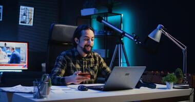 Happy man doing internet shopping, carefully typing credit card information on laptop in apartment. Smiling person adding payment method on website while in living room, camera B photo